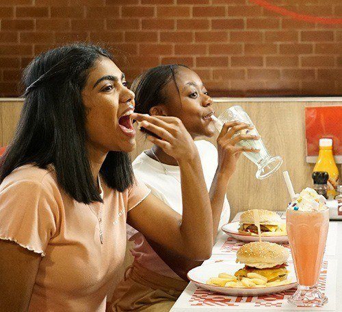 Two young girls eating wimpy burgers and drinking milkshakes