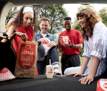 Group of people standing by car looking into Wimpy takeaway bag